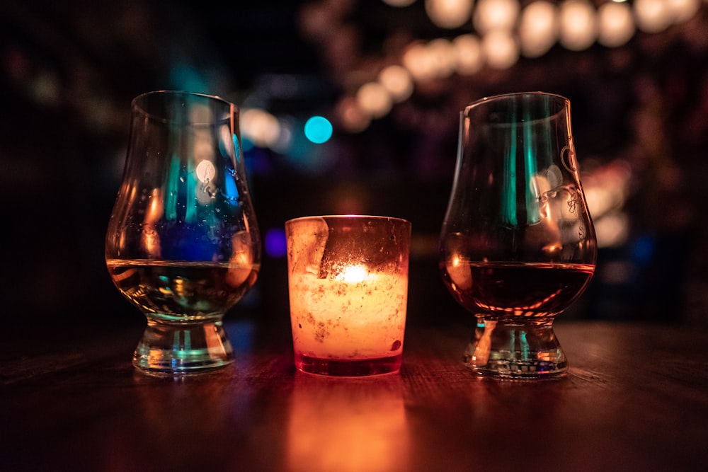 Photographie sélective de deux verres à pied transparent placés près d’une bougie votive sur une table