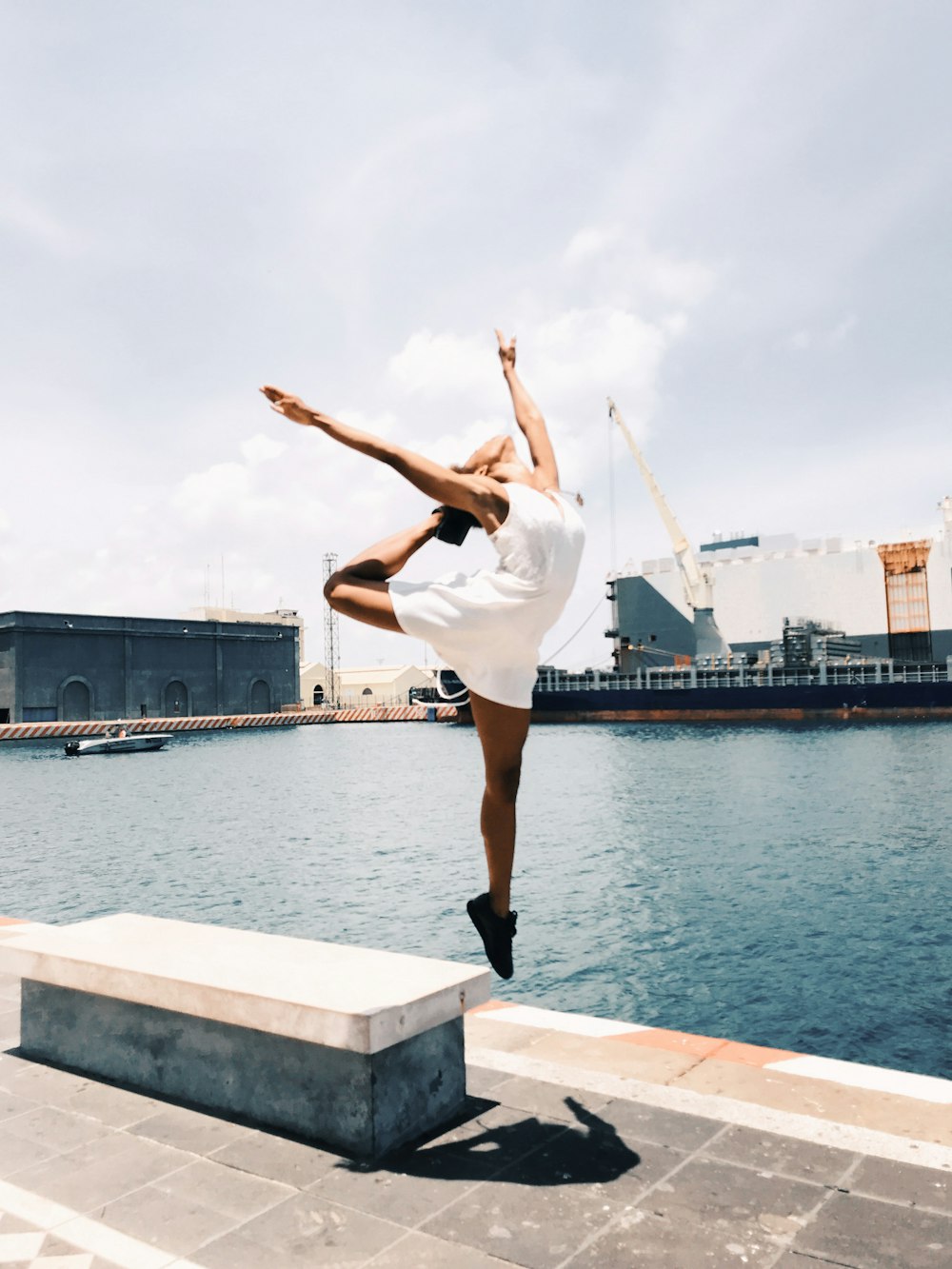 woman jumping in mid-air near body of water during daytime