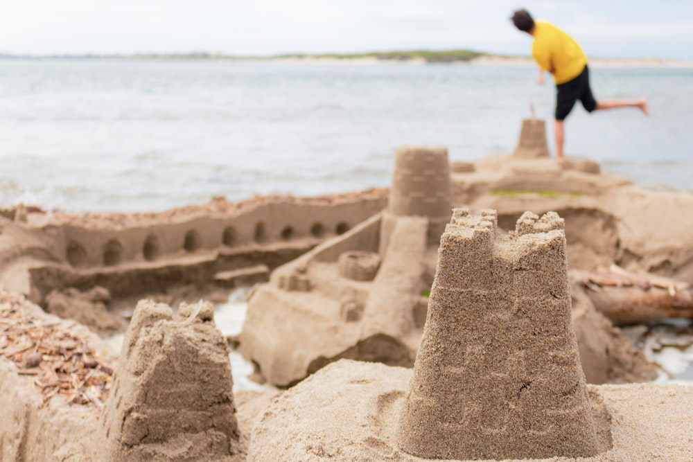 Fotografía de enfoque selectivo del castillo de arena cerca del hombre de pie en la orilla del mar
