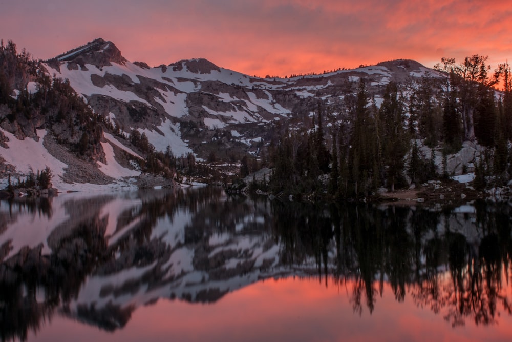 snow covered by mountain near river under sunset