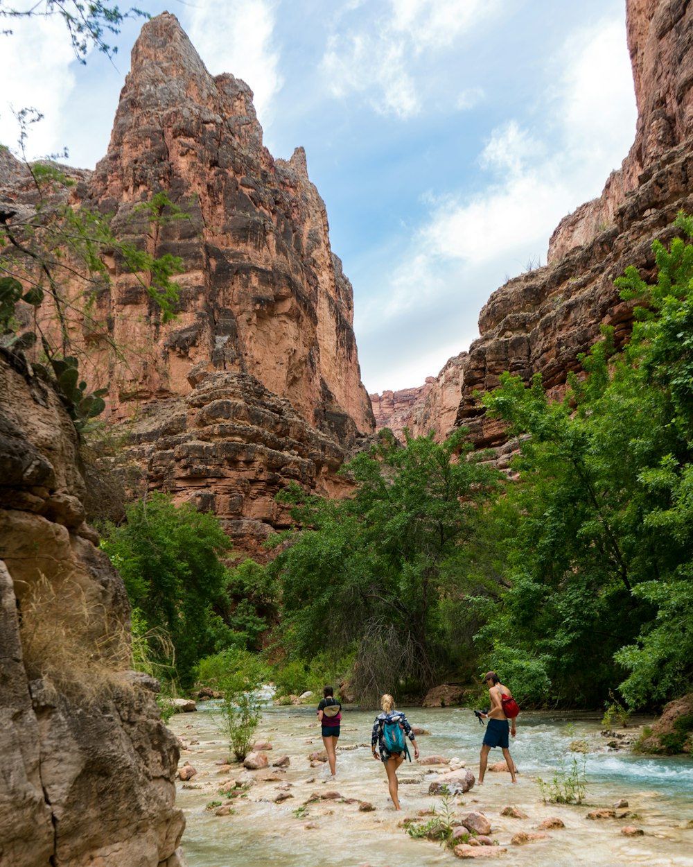 three person walking on the river besides the mountain