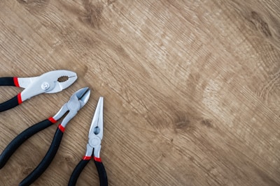 three black handled pliers on brown surface