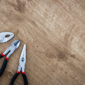 three black handled pliers on brown surface