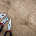 three black handled pliers on brown surface