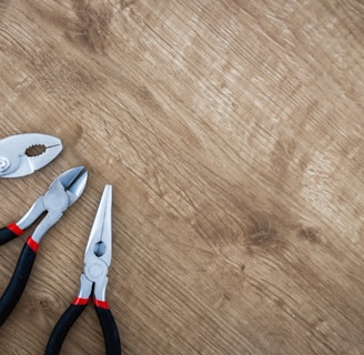 three black handled pliers on brown surface