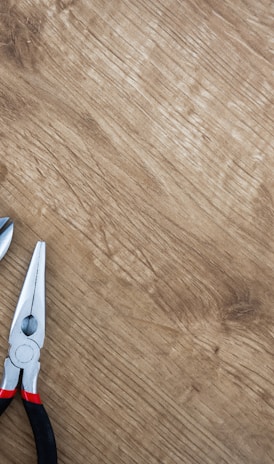 three black handled pliers on brown surface