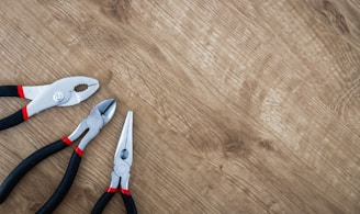 three black handled pliers on brown surface