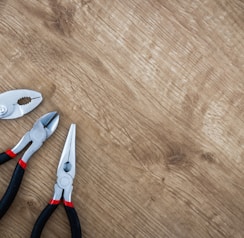 three black handled pliers on brown surface