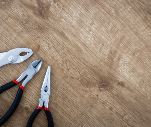 three black handled pliers on brown surface