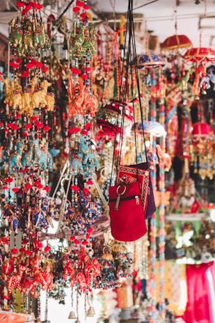A vibrant display of colorful hanging decorations including embroidered cloth elephants, umbrellas, and bags. These items are intricately designed with a myriad of hues, showcasing traditional artistry and craftsmanship with beads and tassels adding to the decorative appeal.