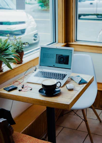 cup of coffee, laptop computer, and red earphones plugged in laptop on brown wooden table