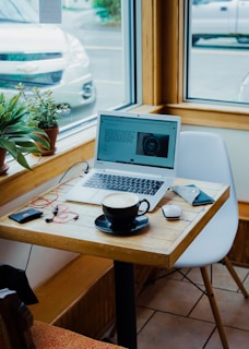 cup of coffee, laptop computer, and red earphones plugged in laptop on brown wooden table