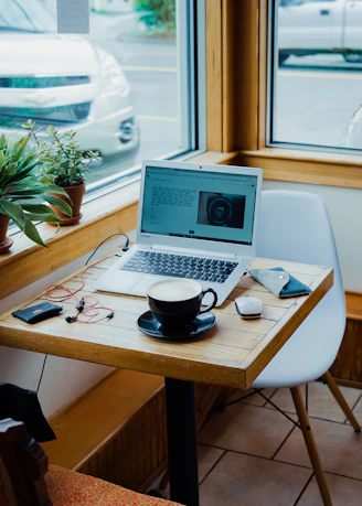 cup of coffee, laptop computer, and red earphones plugged in laptop on brown wooden table