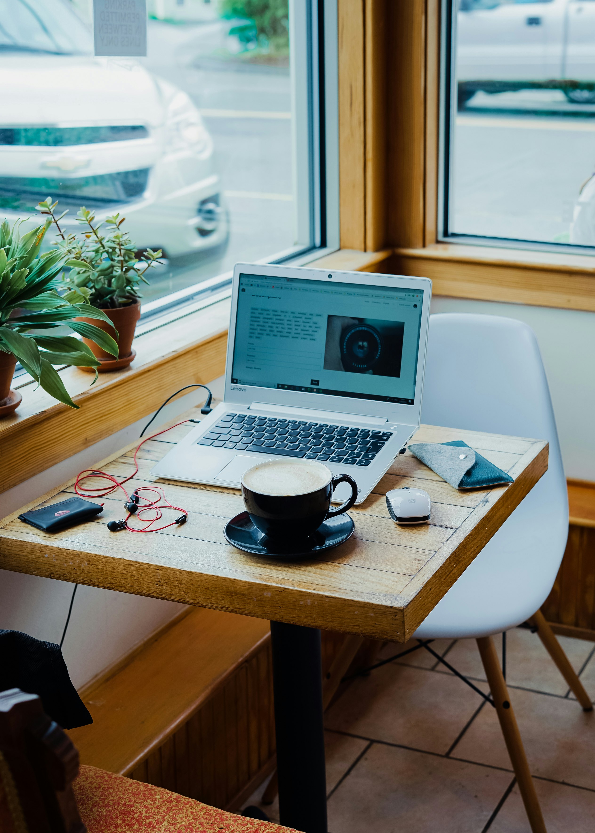 cup of coffee, laptop computer, and red earphones plugged in laptop on brown wooden table