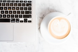 cappuccino on teacup and coaster beside a MacBook