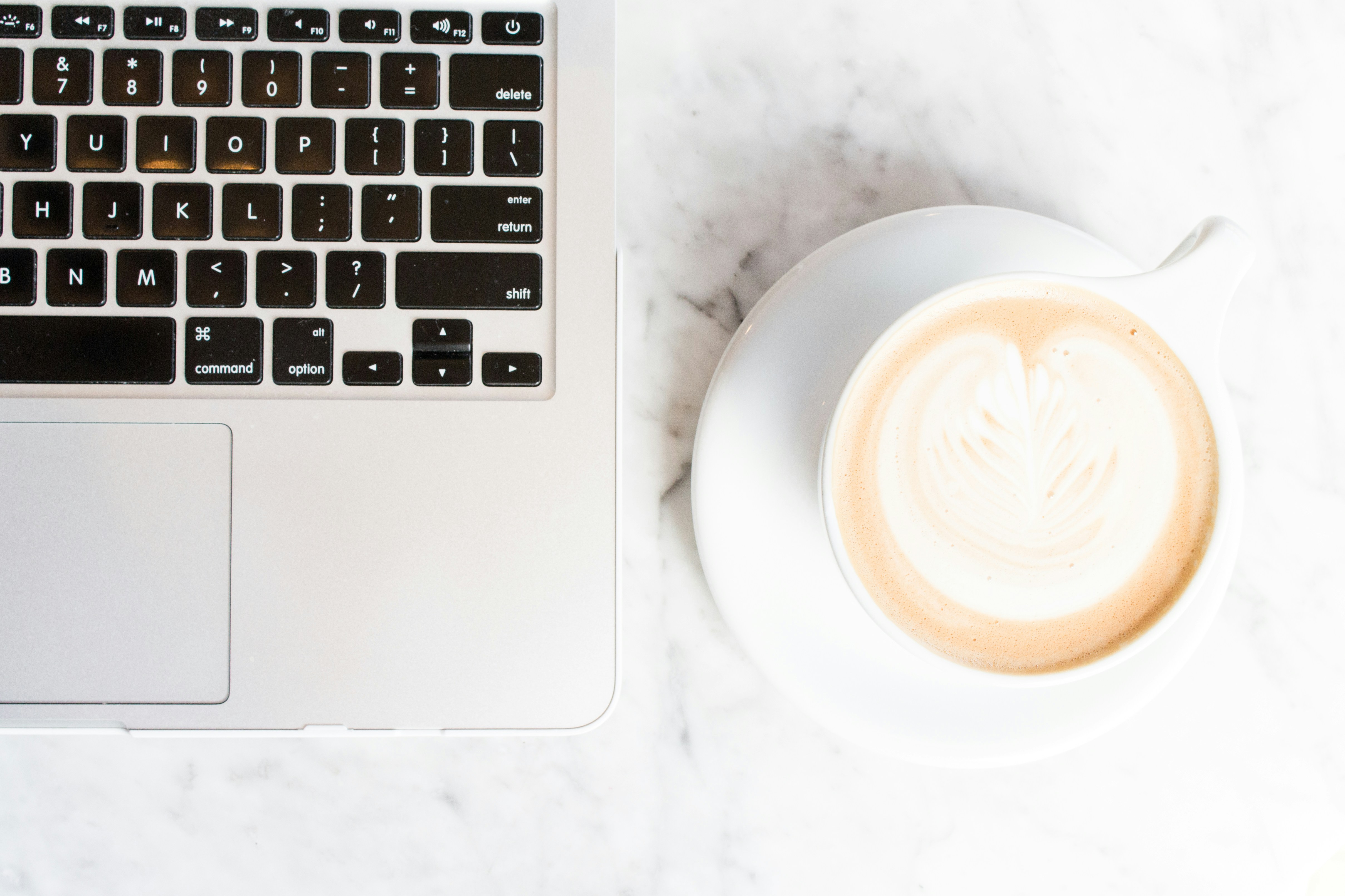 close up view of hands typing on apple macbook keyboard next to coffee cup