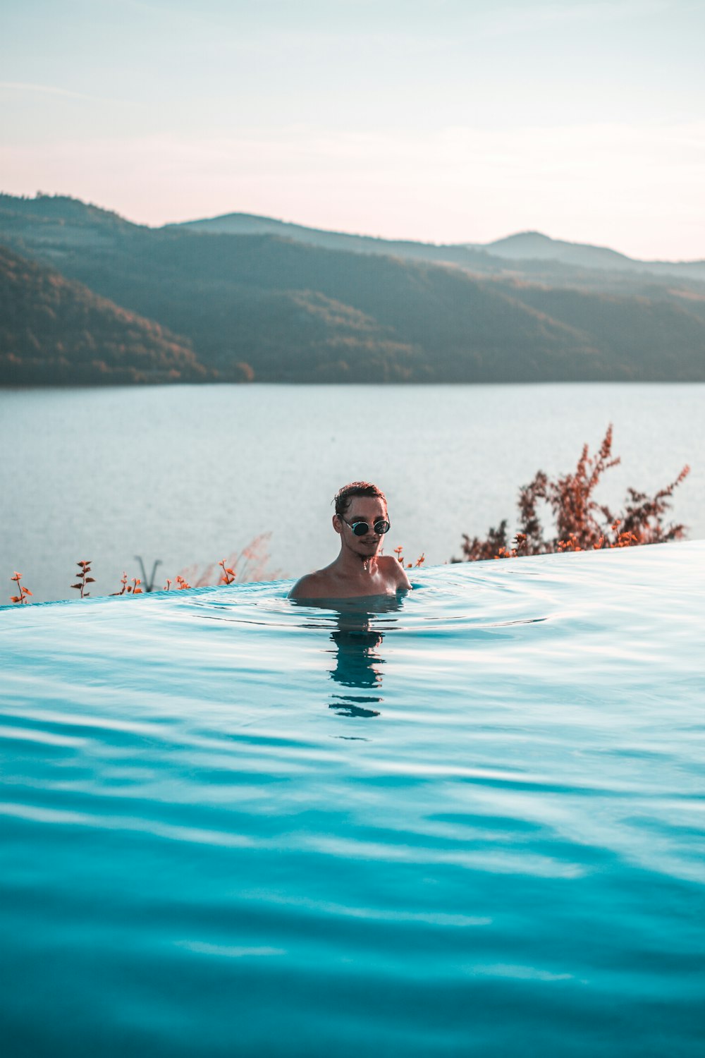 man wearing black sunglasses swimming on infinity pool near body of water at daytime