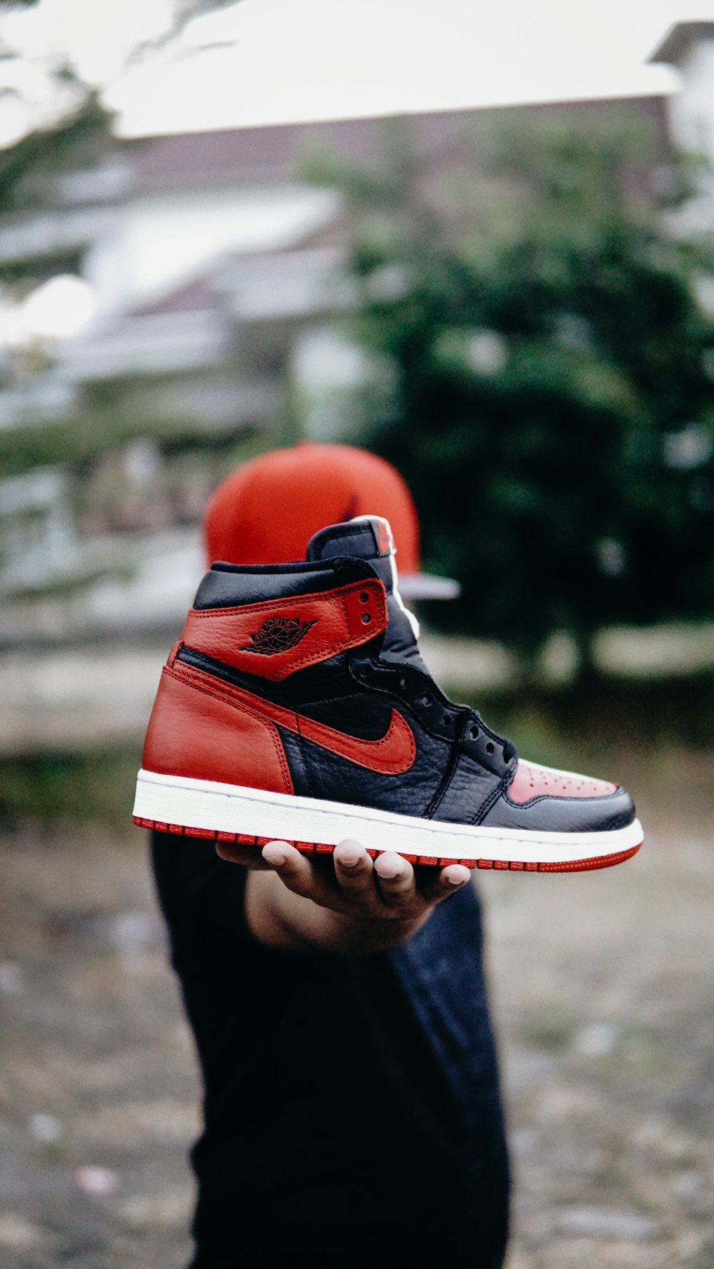 foto di messa a fuoco selettiva di persona che tiene la scarpa Nike Air Jordan 1 nera e rossa spaiata