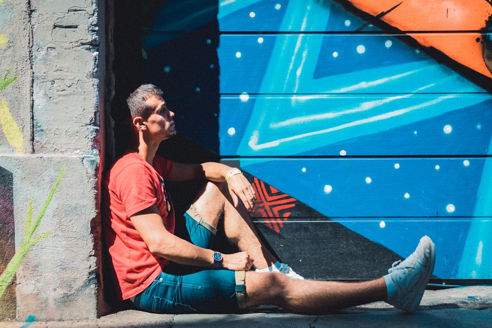 Mann sitzt tagsüber auf dem Boden in der Nähe einer Graffiti-Wand