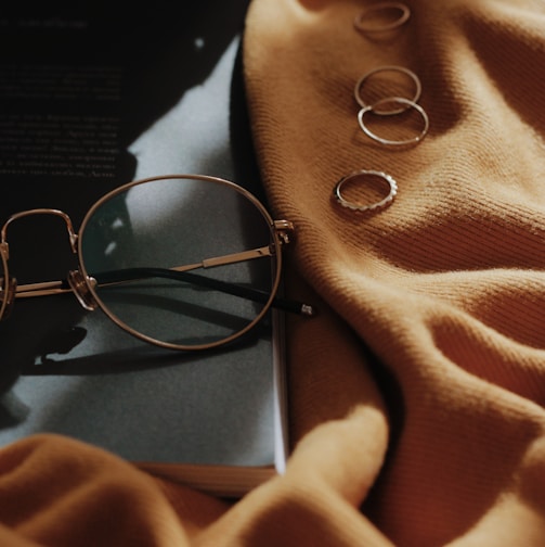 gray framed eyeglasses near four copper-colored accessories on orange sheet