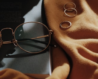 gray framed eyeglasses near four copper-colored accessories on orange sheet