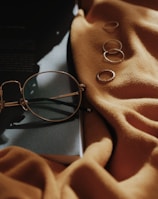 gray framed eyeglasses near four copper-colored accessories on orange sheet