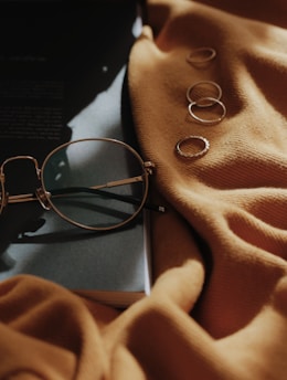 gray framed eyeglasses near four copper-colored accessories on orange sheet