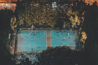 A panoramic view of a well-lit basketball court at night, with players practicing drills.