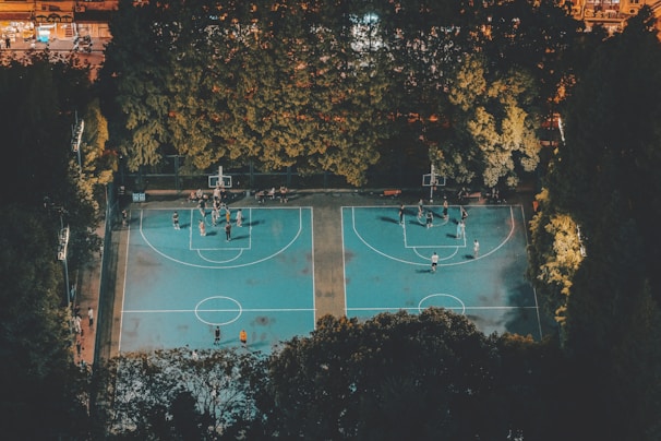 A panoramic view of a well-lit basketball court at night, with players practicing drills.