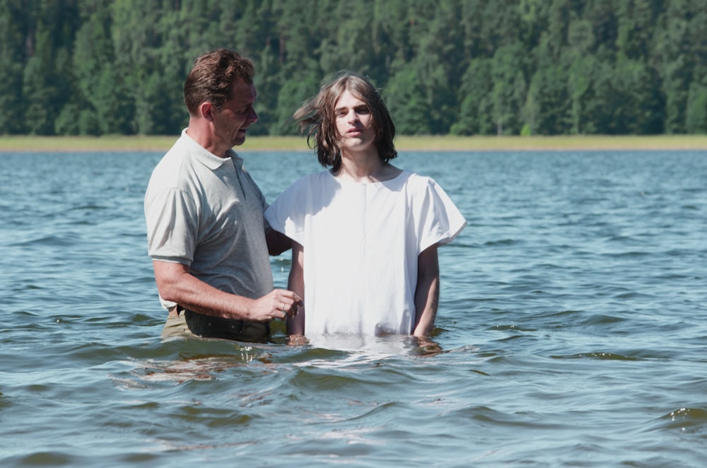 two man standing on body of water near trees at daytime