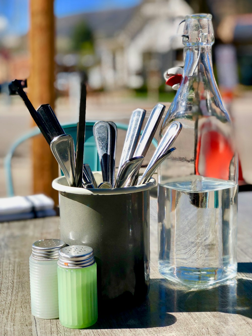 silver-colored cutlery in gray holder with glass bottle on table