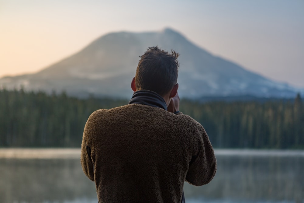 depth of field photography of man in gray sweater standing in front of mountain
