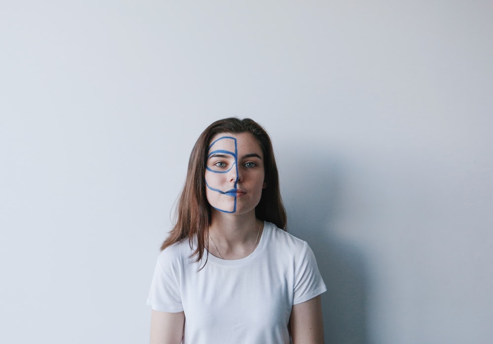 woman wearing white crew-neck t-shirt with mask on face leaning on wall