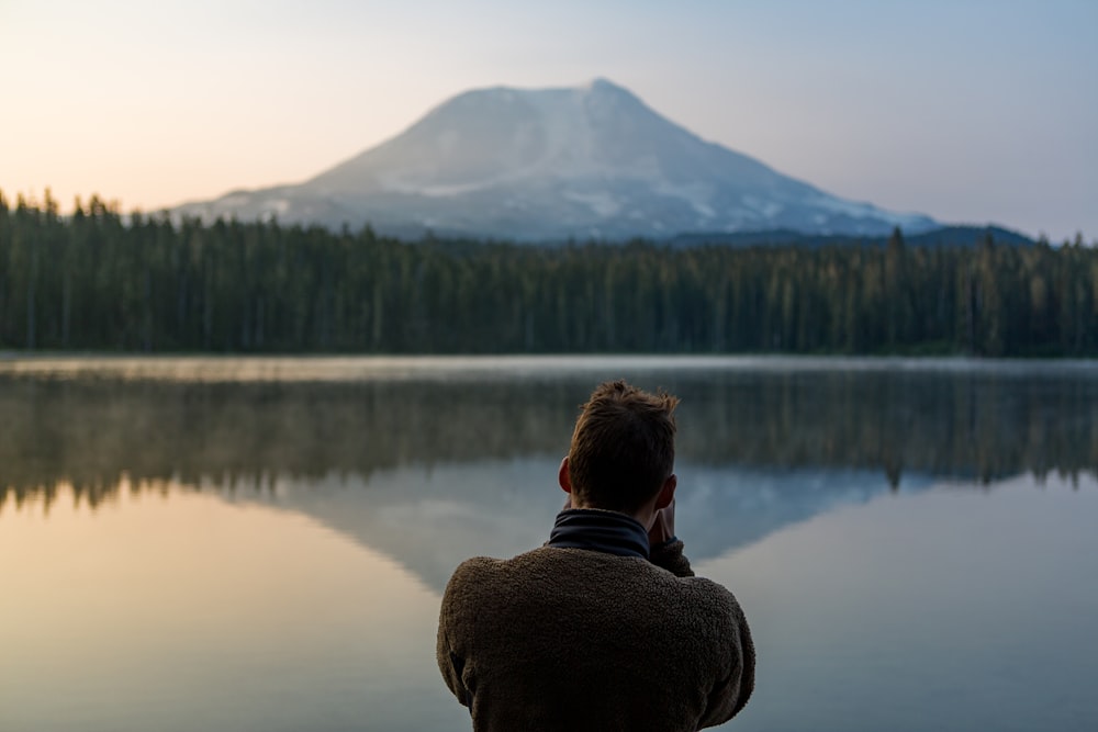 photo of person standing in front of water and forest