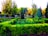 A well-maintained garden with neatly trimmed hedges and a mix of various trees. The vibrant green of the grass and hedges contrasts with the autumnal colors of some trees in the background. Sunlight filters through the leaves, creating a peaceful and serene atmosphere.