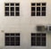 A beige wall with four dark-tinted windows arranged in two rows. Two air conditioning units are mounted on the right side. The surface of the wall has a textured appearance.