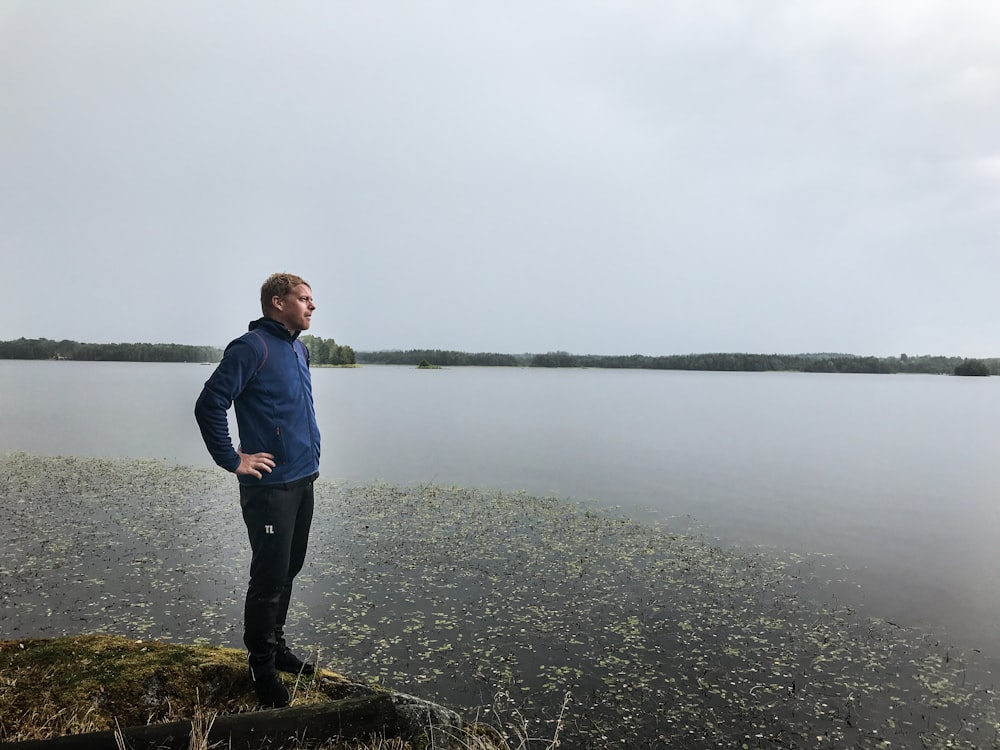 man standing on cliff near body of water