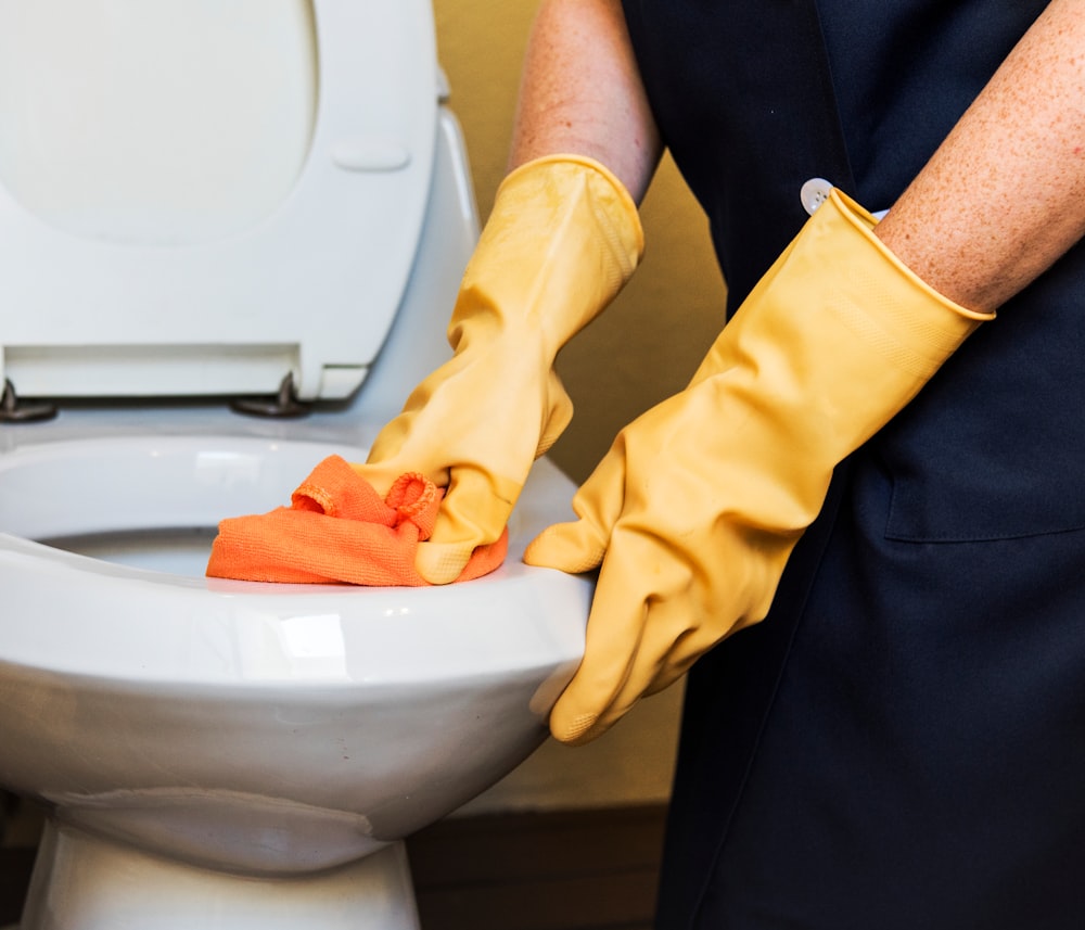 person wearing gloves cleaning toilet bowl