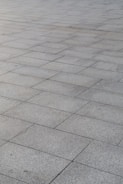 A surface covered with rectangular stone tiles arranged in a grid pattern. The tiles have a light gray color with slight variations in tone, giving a textured look.