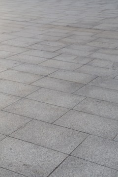 A surface covered with rectangular stone tiles arranged in a grid pattern. The tiles have a light gray color with slight variations in tone, giving a textured look.