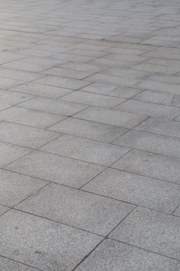 A surface covered with rectangular stone tiles arranged in a grid pattern. The tiles have a light gray color with slight variations in tone, giving a textured look.