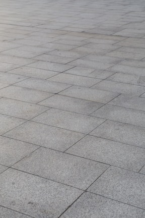 A surface covered with rectangular stone tiles arranged in a grid pattern. The tiles have a light gray color with slight variations in tone, giving a textured look.