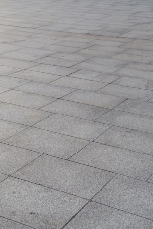 A surface covered with rectangular stone tiles arranged in a grid pattern. The tiles have a light gray color with slight variations in tone, giving a textured look.