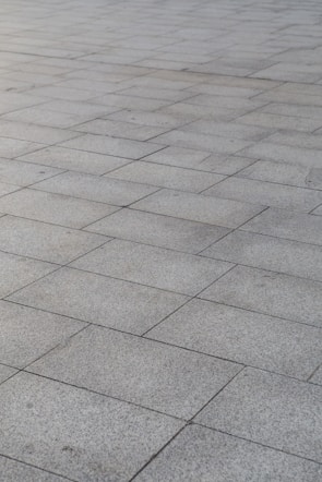 A surface covered with rectangular stone tiles arranged in a grid pattern. The tiles have a light gray color with slight variations in tone, giving a textured look.