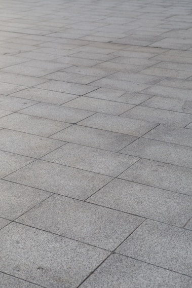 A surface covered with rectangular stone tiles arranged in a grid pattern. The tiles have a light gray color with slight variations in tone, giving a textured look.