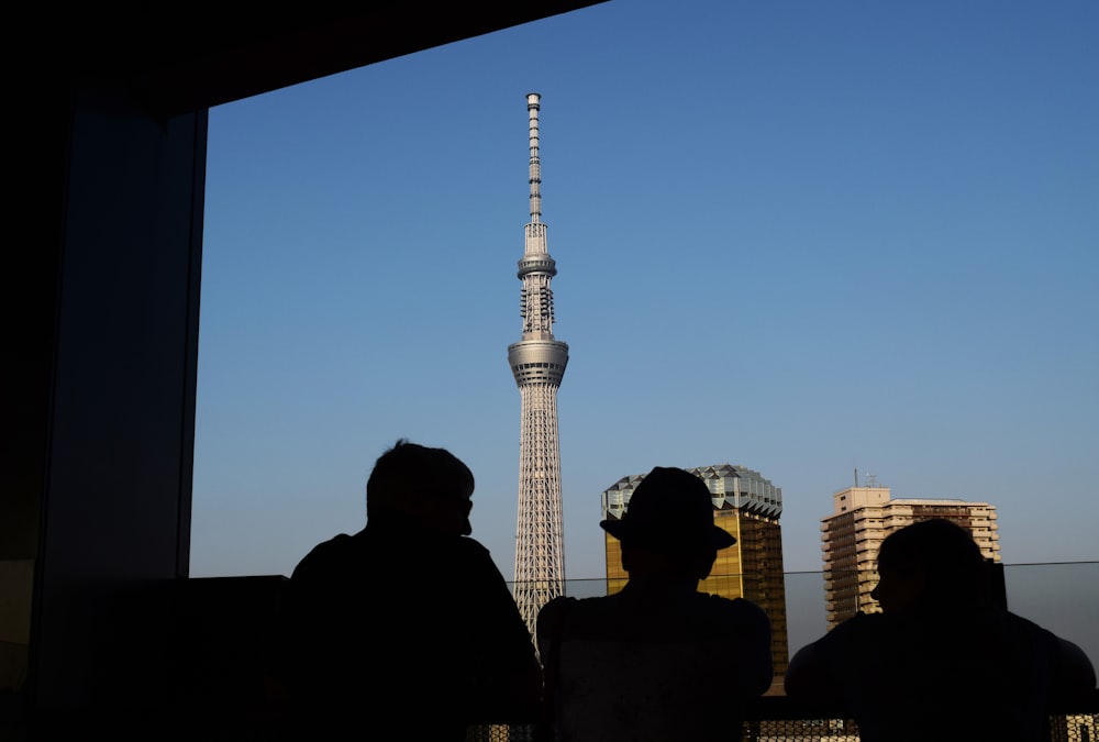 three silhouette of persons standing in front window watching tower building