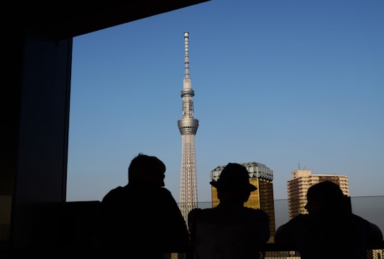 three silhouette of persons standing in front window watching tower building in Sensō-ji Japan