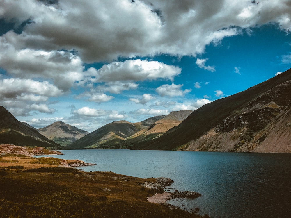 large body of water across mountains under white and blue cloudy skies