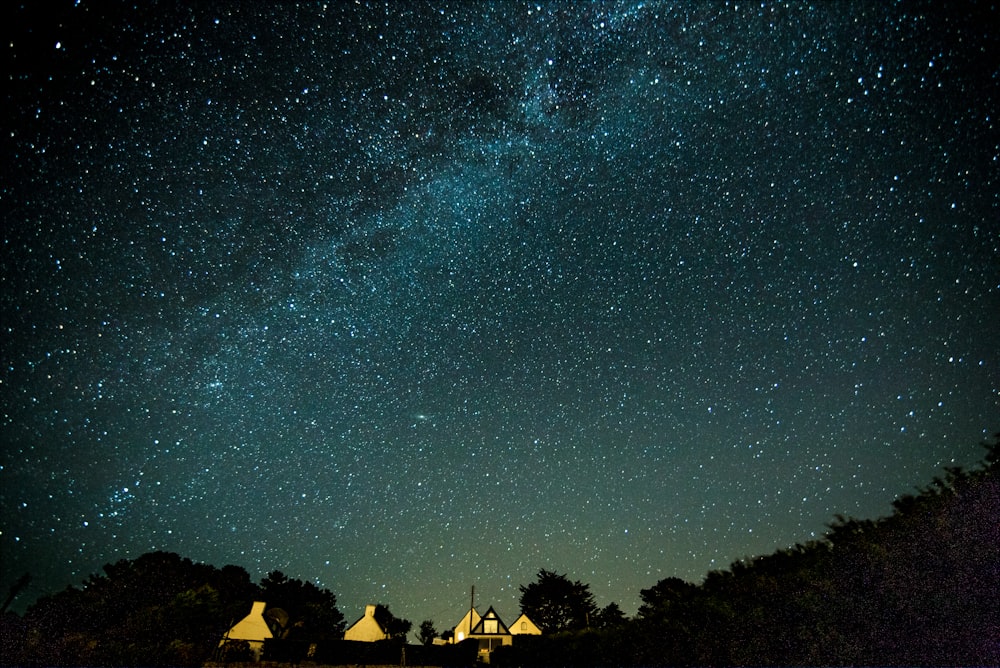 lighted house under sky with stars at night