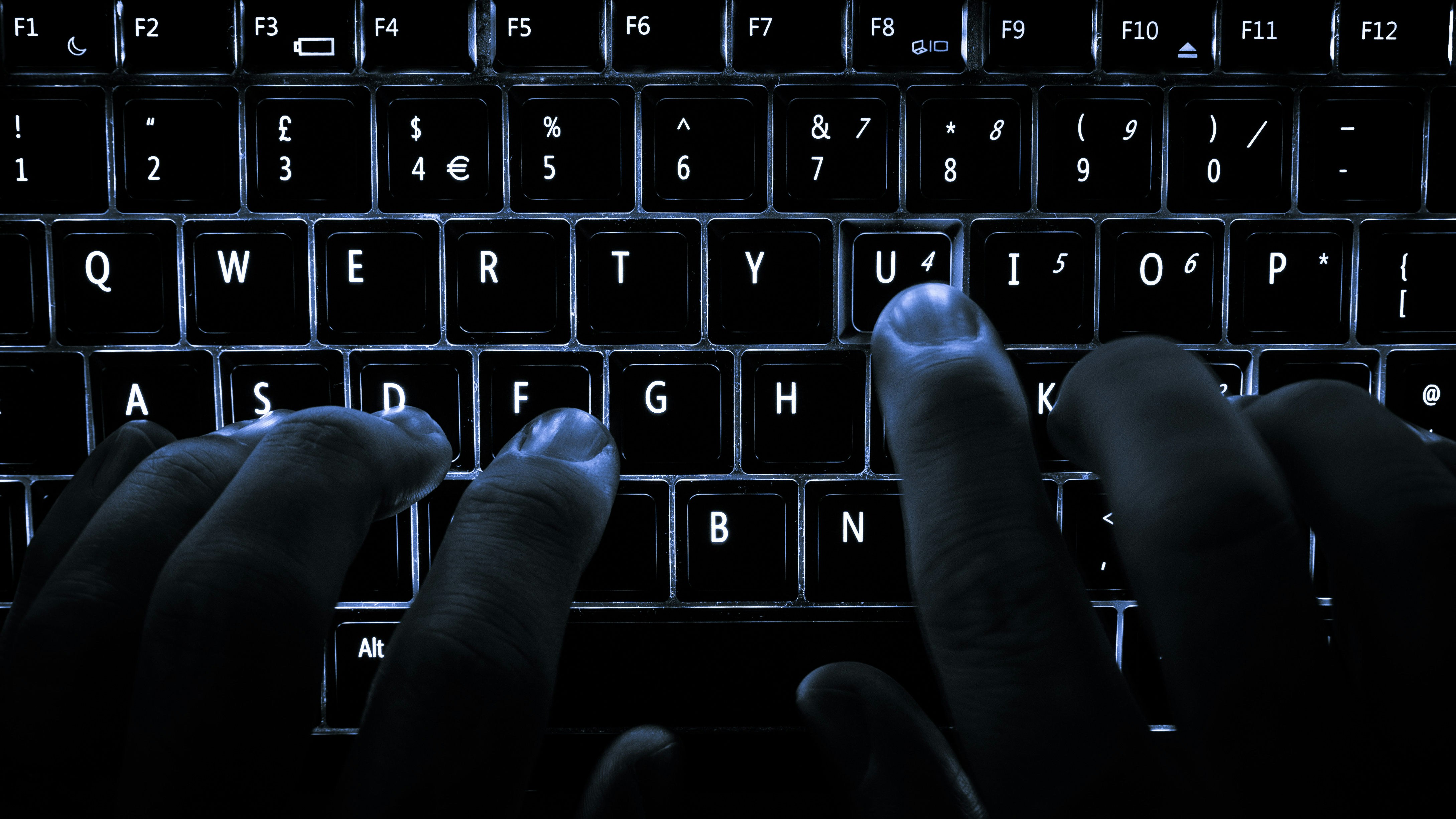 Close-up of a developer’s hands typing rapidly on a backlit keyboard in a dimly lit room.